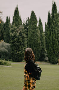 Side view of woman with backpack standing on land against trees