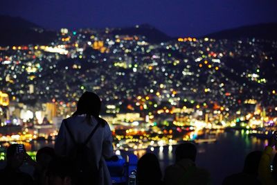 Rear view of woman against illuminated city at night