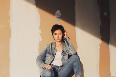 Portrait of young woman with short hair crouching against wall