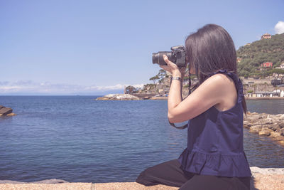 Woman photographing sea against sky