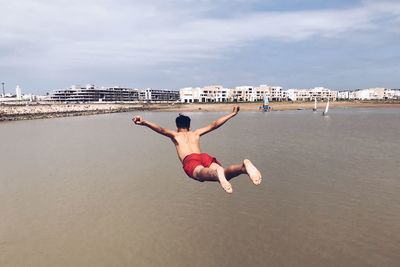 Full length of shirtless man jumping on beach