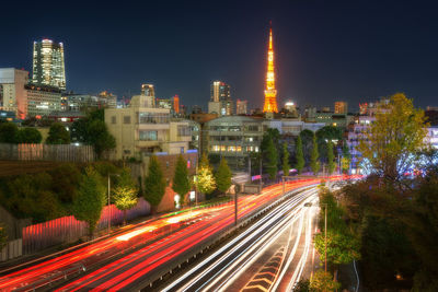 Light trails on street amidst illuminated buildings against sky at night