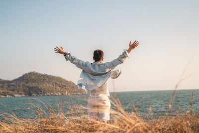 Rear view of man with arms outstretched standing at sea against clear sky