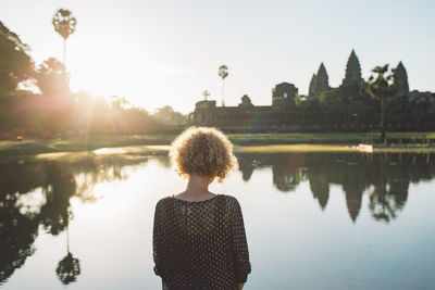 Rear view of woman standing by lake against sky