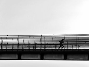 Silhouette man walking on bridge against clear sky