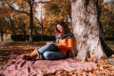 Young woman sitting on tree trunk during autumn