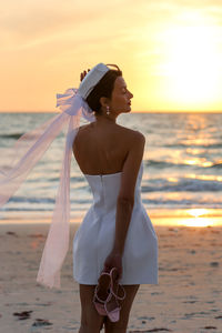 Side view of woman standing at beach during sunset