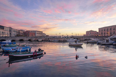 Boats moored in canal by buildings against sky during sunset