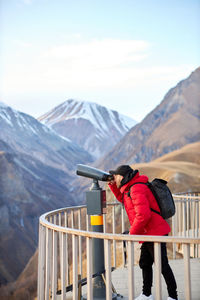 Young man with black backpack looking on observation deck, tourist traveler on background