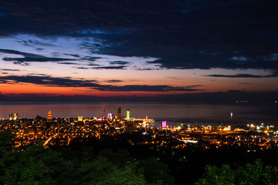 High angle view of illuminated city by sea against sky