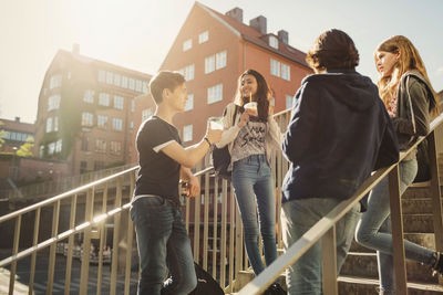 Teenagers talking while having drinks on steps in city