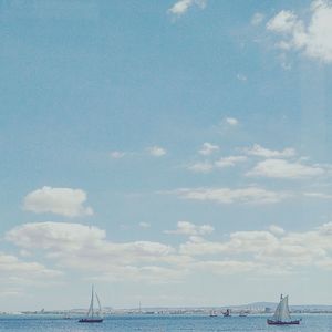 Boats sailing in sea against cloudy sky