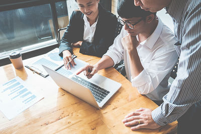 Colleagues using laptop at desk in office