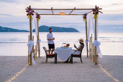 Man standing on table by sea against sky