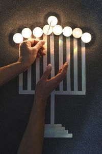 A woman's hand lights candles in a stylized candlestick on a table, jewish holiday of hanukkah,