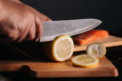 Cropped hand cutting lemon on board against black background