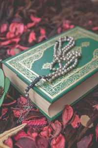 Close-up of koran with prayer beads and flowers on table
