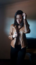 Young woman wearing brown leather jacket while standing against wall