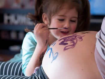 Smiling girl painting pregnant mother belly at home