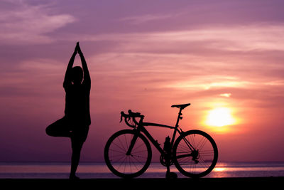 Silhouette man with bicycle in sea against sky during sunset