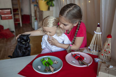 Cute girl playing with doll while petting cat at home