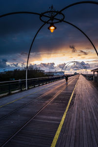 Footbridge against cloudy sky during sunset