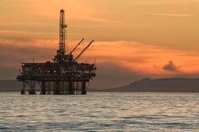 Silhouette oilplatform oilrig in sea against sky during sunset