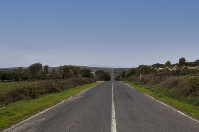 Road amidst field against clear sky