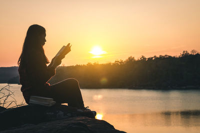 Silhouette man sitting by lake against sky during sunset