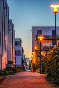 Illuminated street amidst buildings against sky at sunset