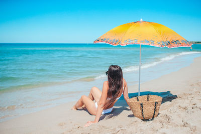 Rear view of woman with umbrella at beach against clear sky