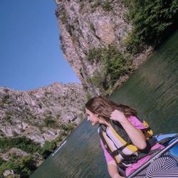 Young woman on rock by tree against clear sky