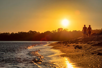 People on beach against sky during sunset