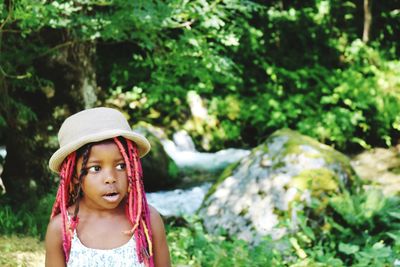 Cute girl with dreadlocks looking away while standing against plants