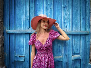 Blonde woman wearing pink summer dress and ha standing against a blue wooden door