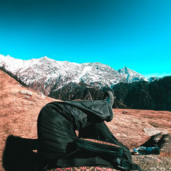 Man sitting on snowcapped mountain against blue sky