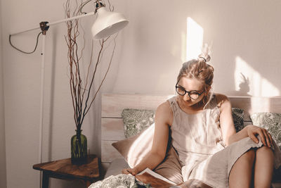 Woman reading book while sitting on bed at home
