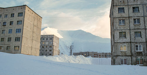 Snow covered buildings by mountain against sky