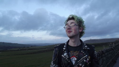 Man looking away while standing against cloudy sky