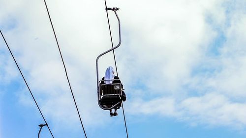 Low angle view of woman sitting in ski lift against cloudy sky