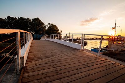 Footpath by railing against sky during sunset