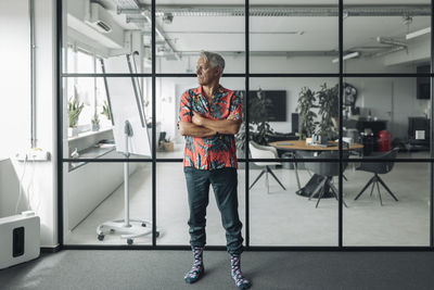 Businessman wearing casual standing with arms crossed against glass wall at office