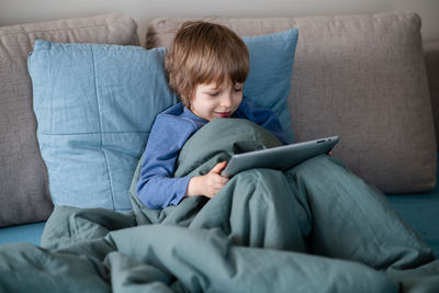 Boy laying in bed and communicating with grandma via video chat using laptop during coronavirus