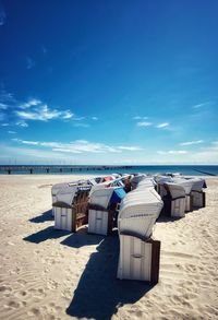 Hooded chairs on beach against blue sky