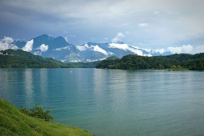 Scenic view of lake by mountains against cloudy sky