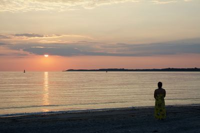 Rear view of woman standing on shore at beach during sunset