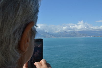 Close-up of woman photographing sea against sky
