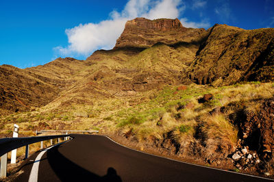 Road by rocky mountains against cloudy sky