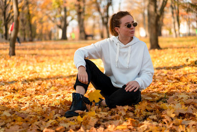 Young woman sitting on leaves during autumn