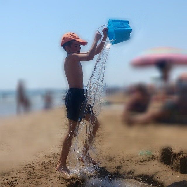 beach, sand, focus on foreground, metal, water, rope, sea, shore, close-up, clear sky, day, selective focus, outdoors, sunlight, swing, incidental people, metallic, childhood